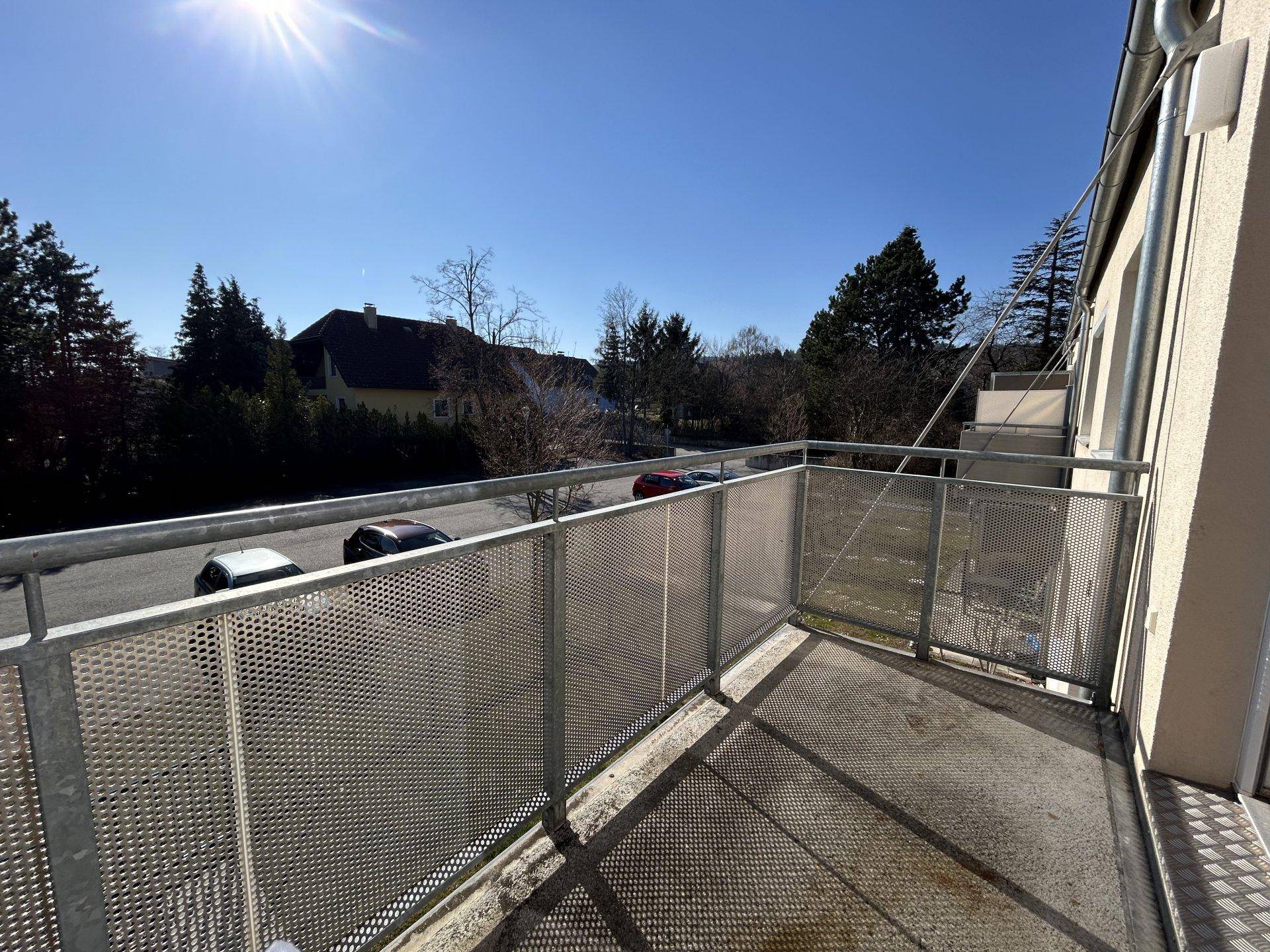 Leerer Balkon mit Metallgeländer und Blick auf die Umgebung an einem sonnigen Tag.