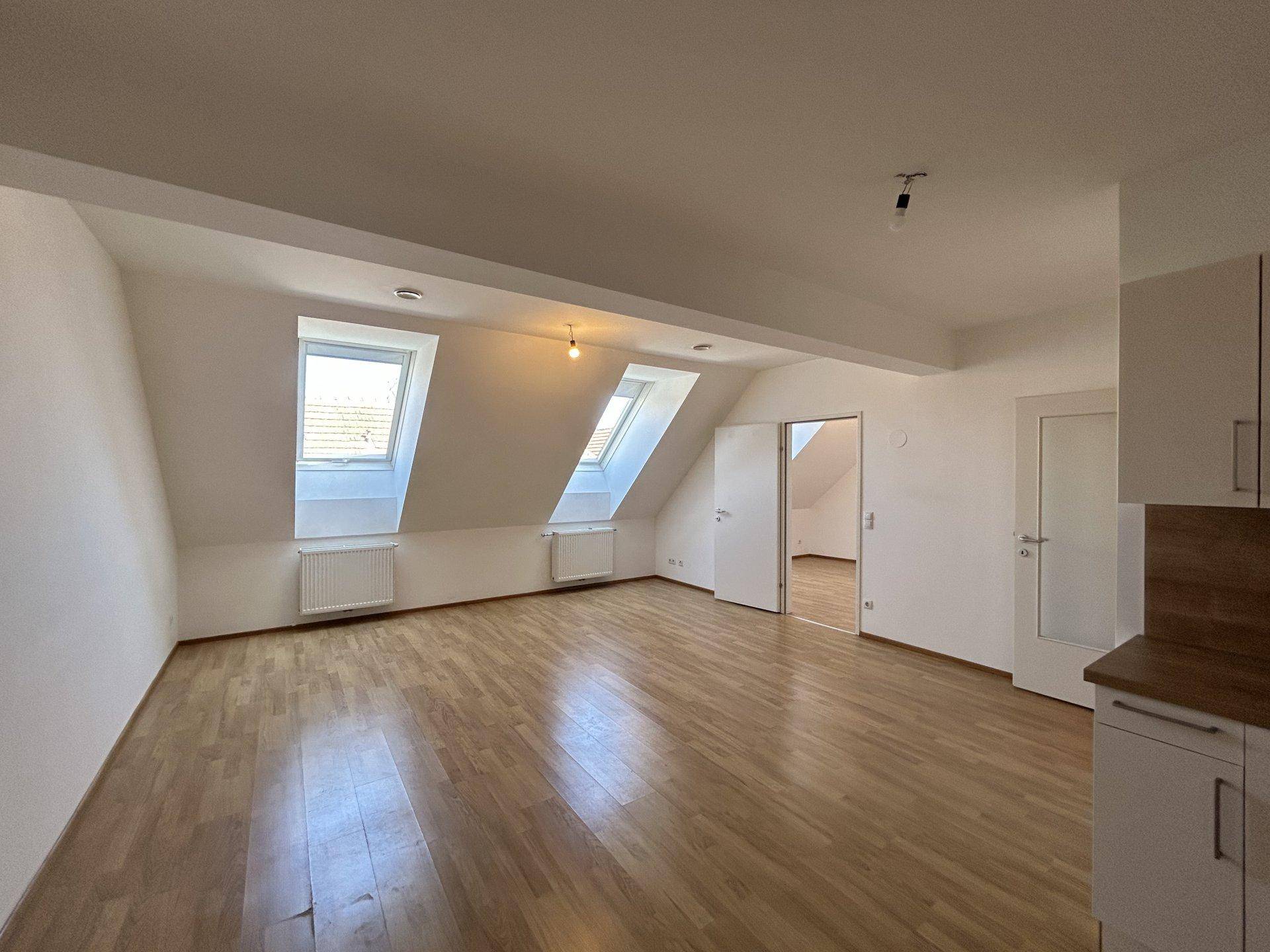 Heller Wohnraum im Dachgeschoss mit Holzboden, Dachfenstern und Heizkörpern.