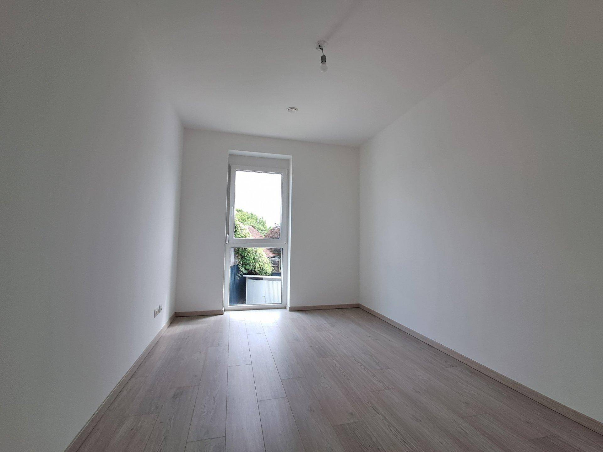 Heller Raum mit Laminatboden und großem Fenster, das viel Tageslicht hereinlässt.