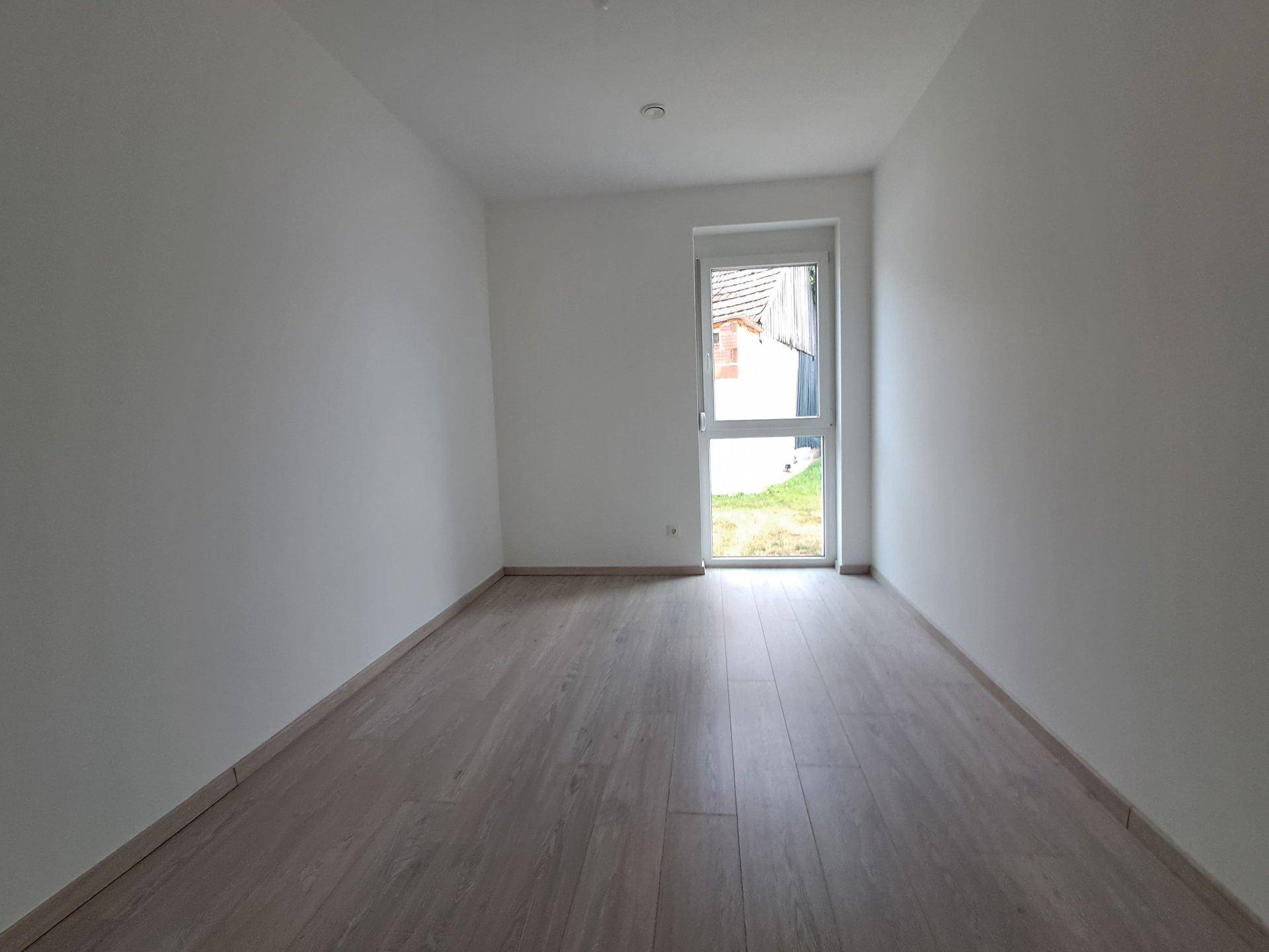 Helles Schlafzimmer mit Laminatboden und Zugang zu einem kleinen Außenbereich.