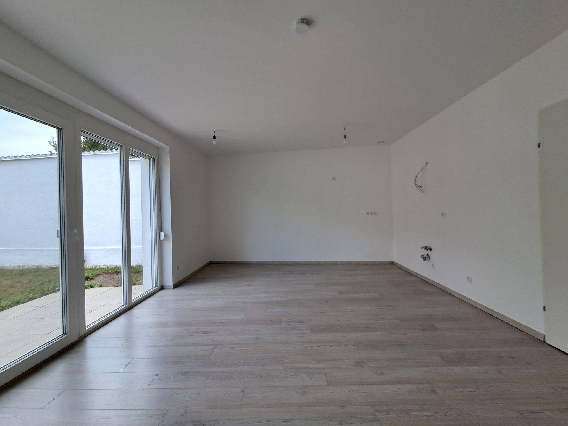 Heller, leerer Raum mit großen Schiebetüren zum Garten und modernem Laminatboden.
