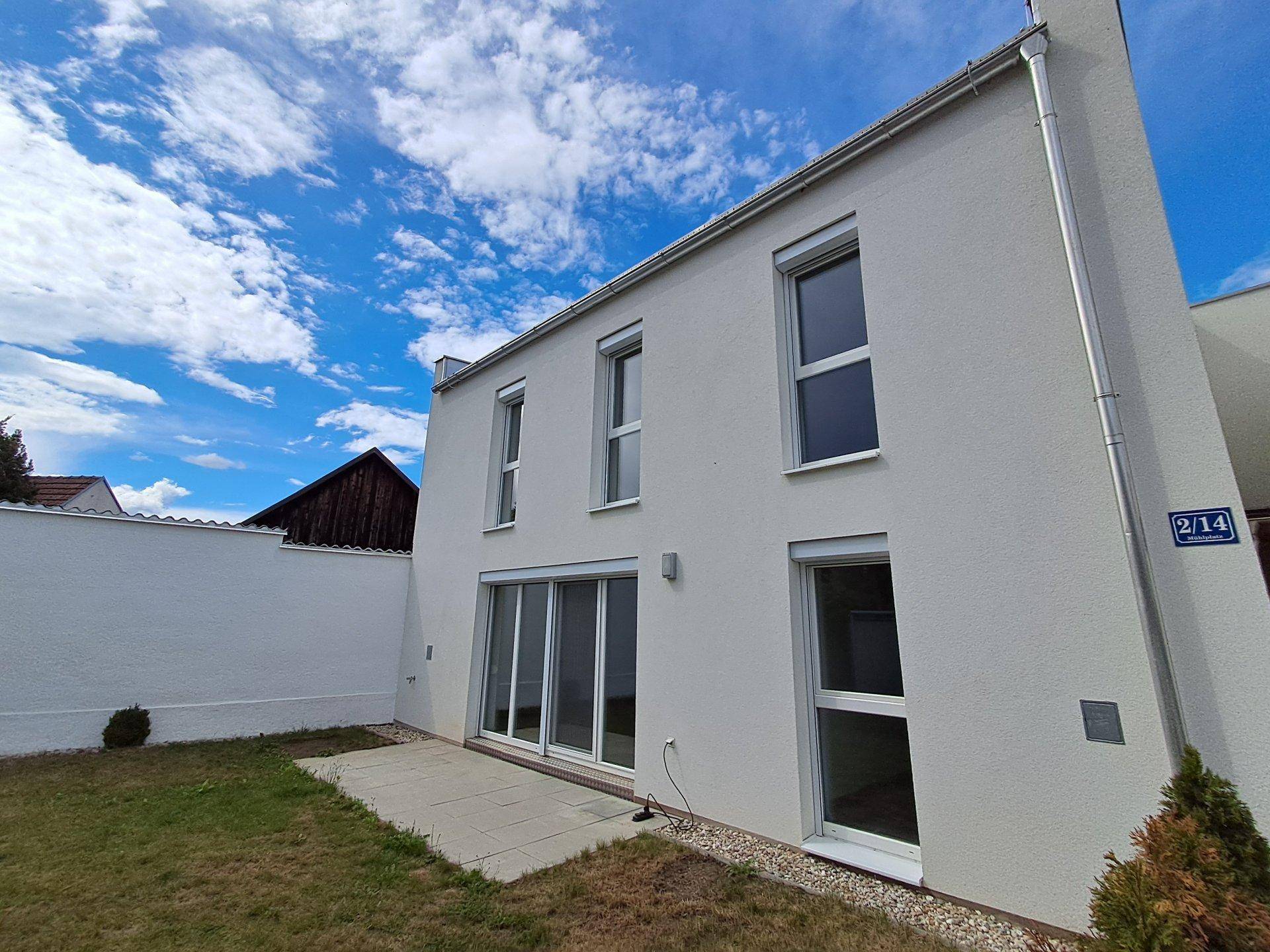 Moderne Hausfassade mit großen Fenstern, Schiebetüren und einer kleinen Terrasse.