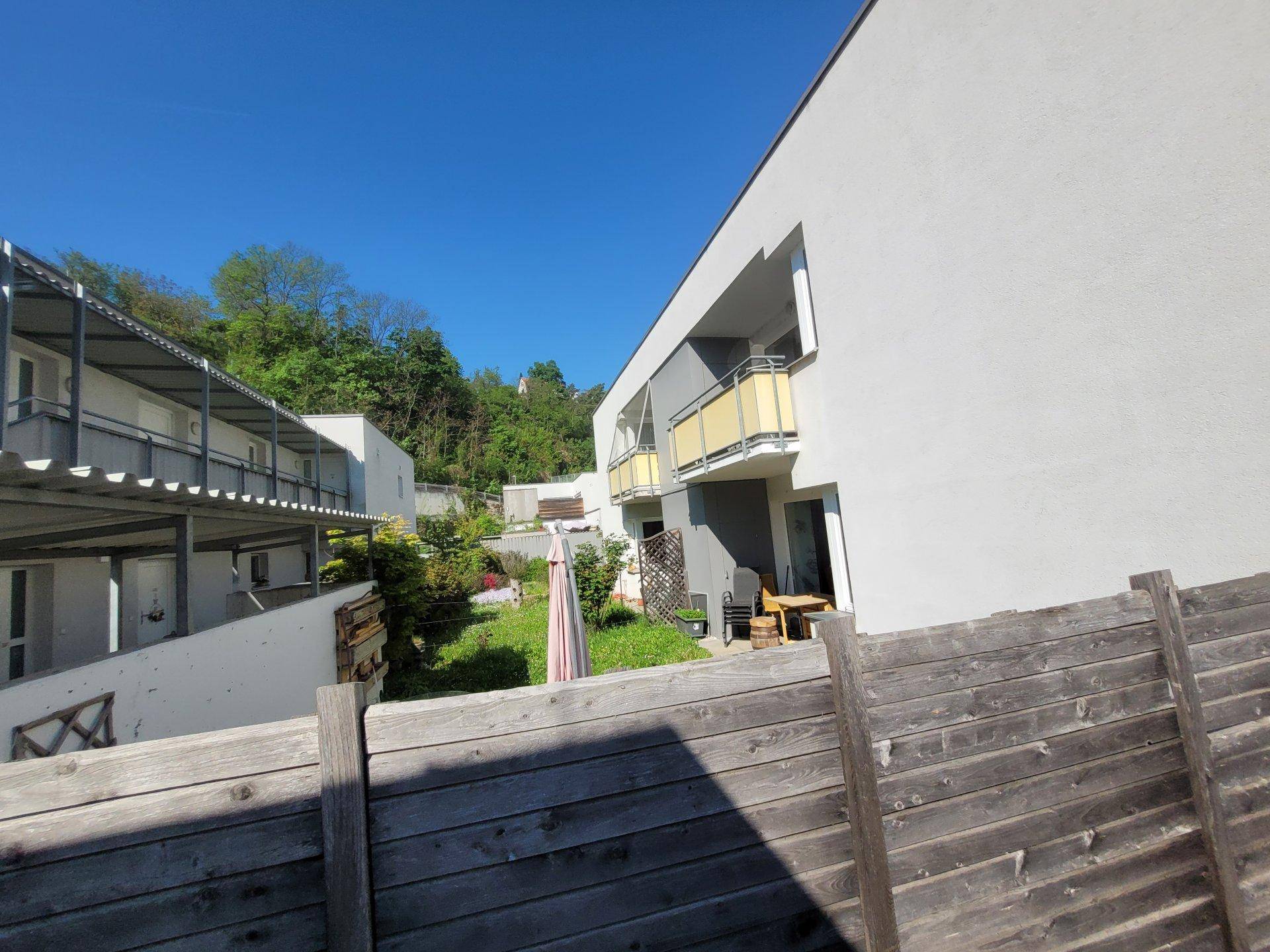 Gebäude mit Balkonen und einem kleinen Gartenbereich, umgeben von einem Holzzaun.
