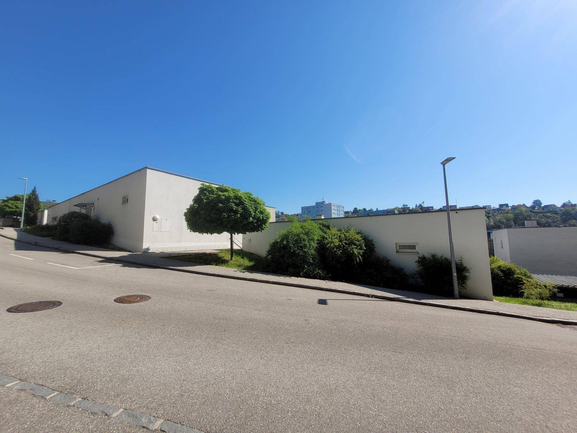 Moderne weiße Gebäude entlang einer Straße mit grüner Bepflanzung unter blauem Himmel.