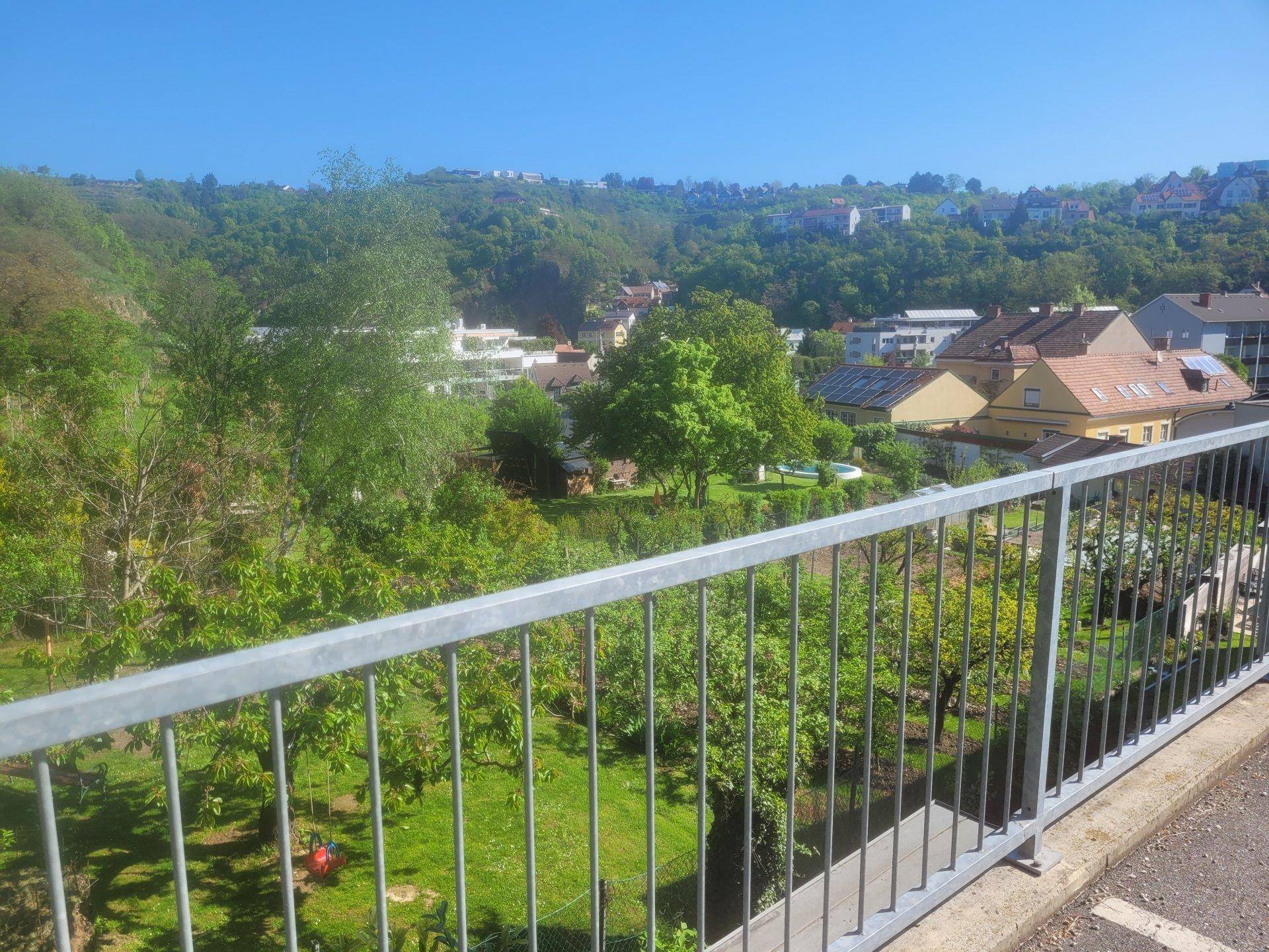 Blick von einem Balkon oder einer Terrasse auf ein grünes Tal mit Häusern und Bäumen.