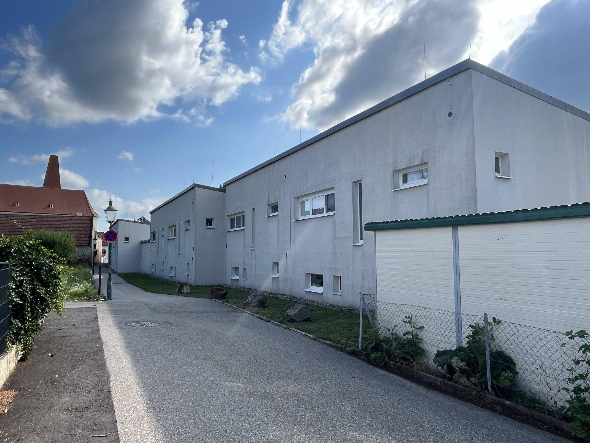 Moderne Wohngebäude mit schlichter Fassade, kleinen Fenstern und flachem Dach entlang einer ruhigen Straße.