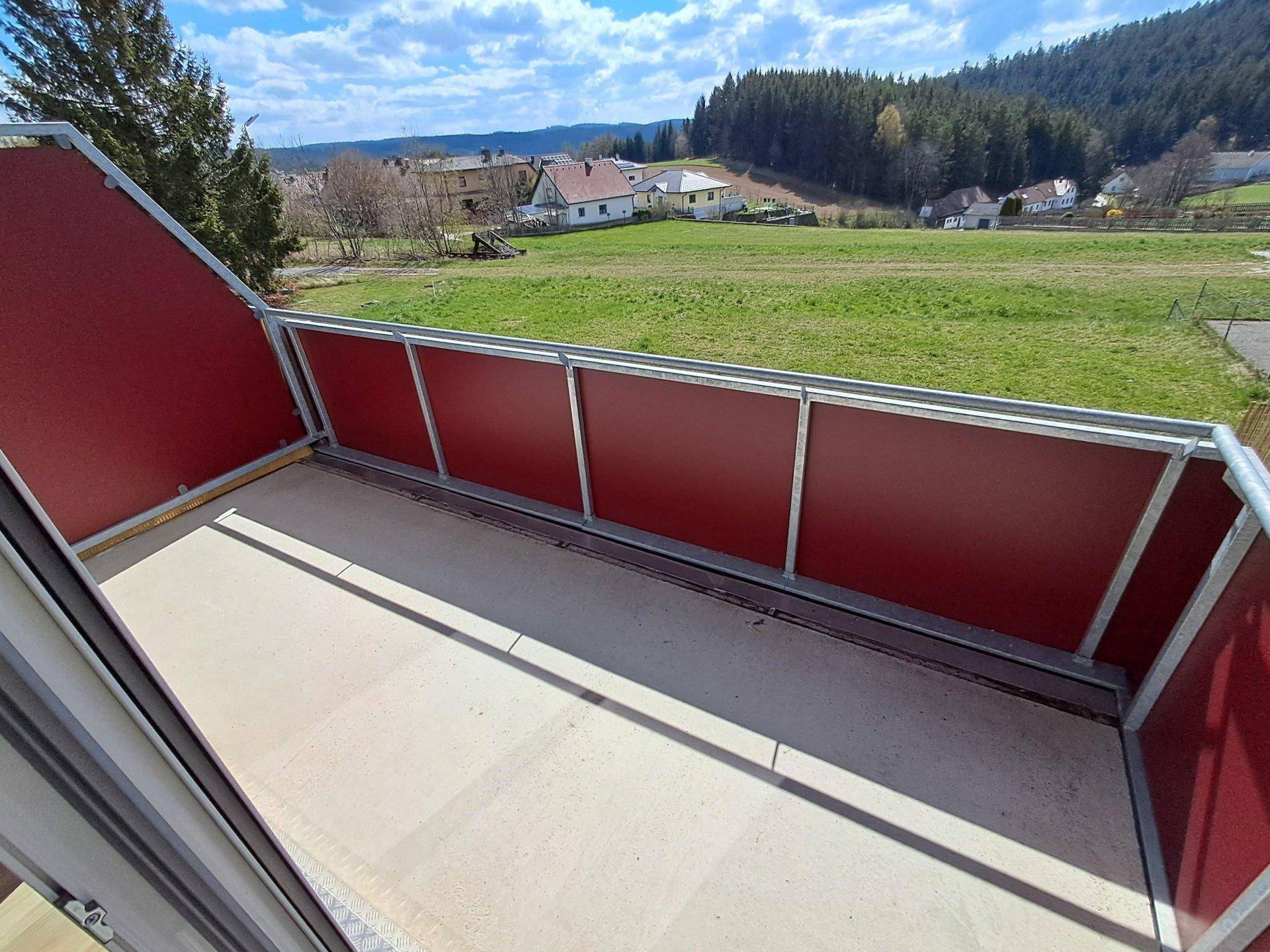 Geräumiger Balkon mit rotem Geländer und weitem Blick über grüne Felder und die Landschaft.