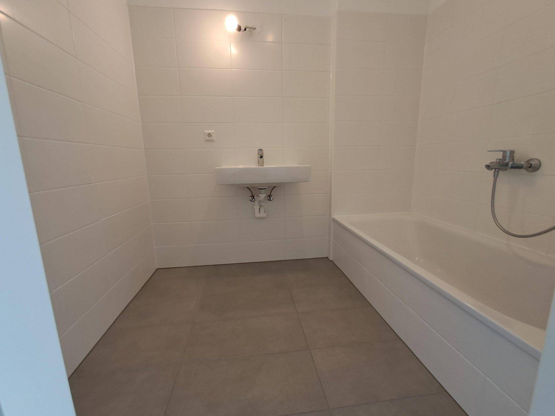 Modernes Badezimmer mit weißen Fliesen, grauen Bodenfliesen, Waschbecken und Badewanne.