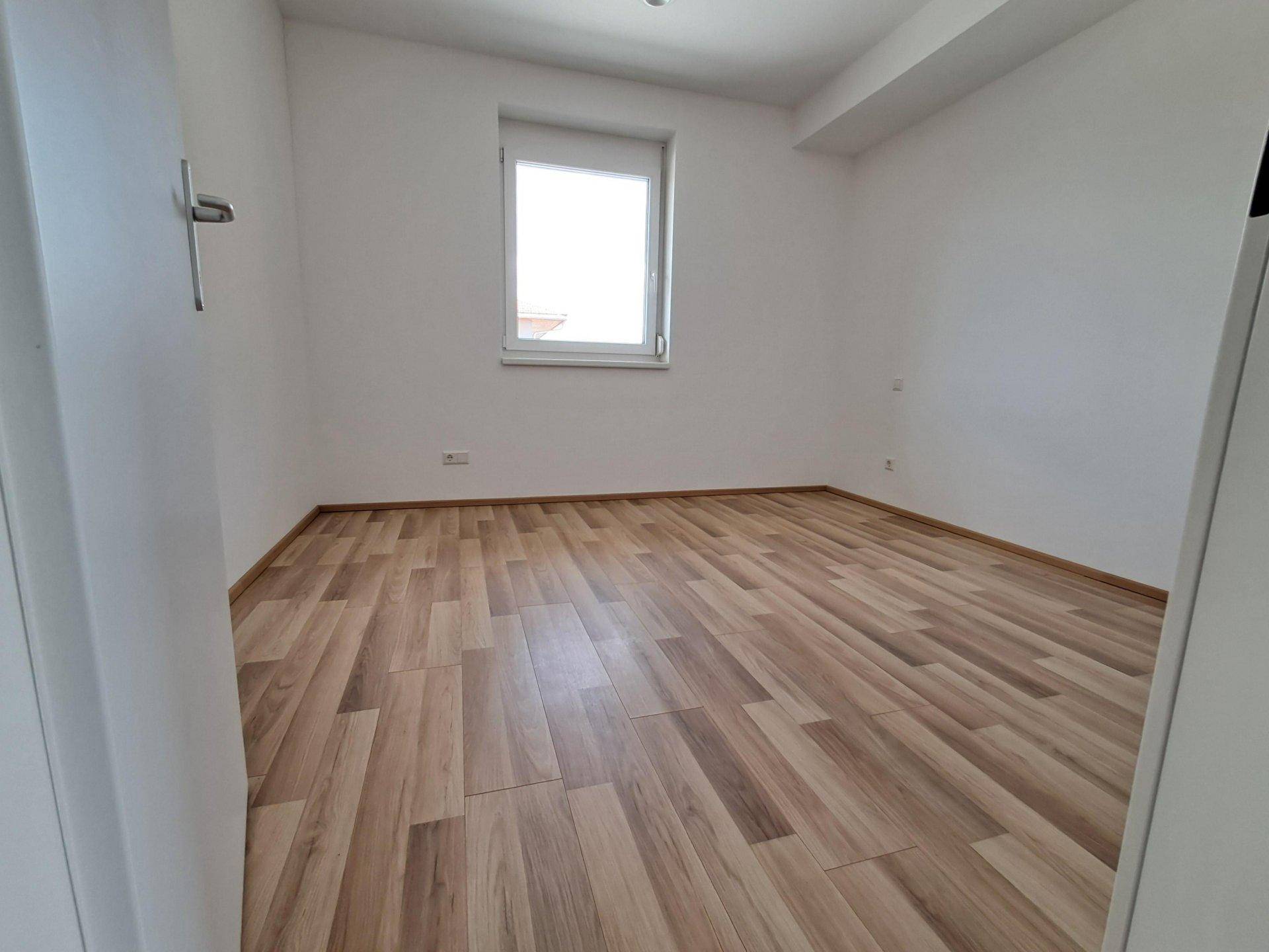 Geräumiges, helles Schlafzimmer mit Laminatboden und weißen Wänden, bereit zum Einrichten.