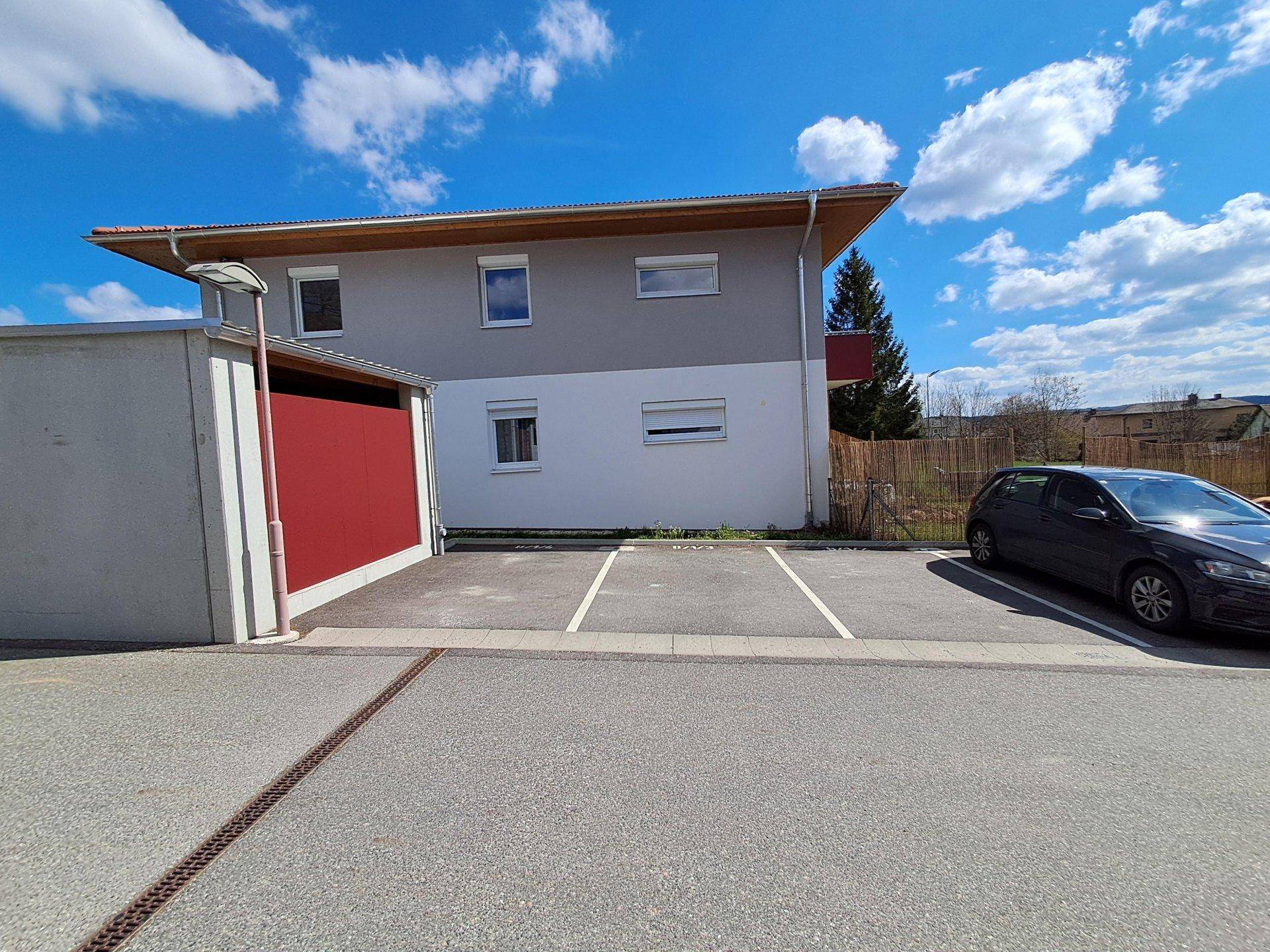 Seitenansicht des Gebäudes mit Parkplätzen im Vordergrund und einer modernen Fassade.