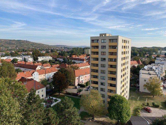 Panoramablick auf das Hochhaus und die umliegende Wohnsiedlung mit Hügeln im Hintergrund.