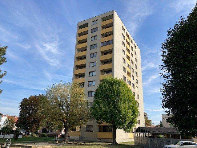 Mehrstöckiges Wohnhaus mit gelben Balkonen, umgeben von Bäumen und einem kleinen Spielplatz.