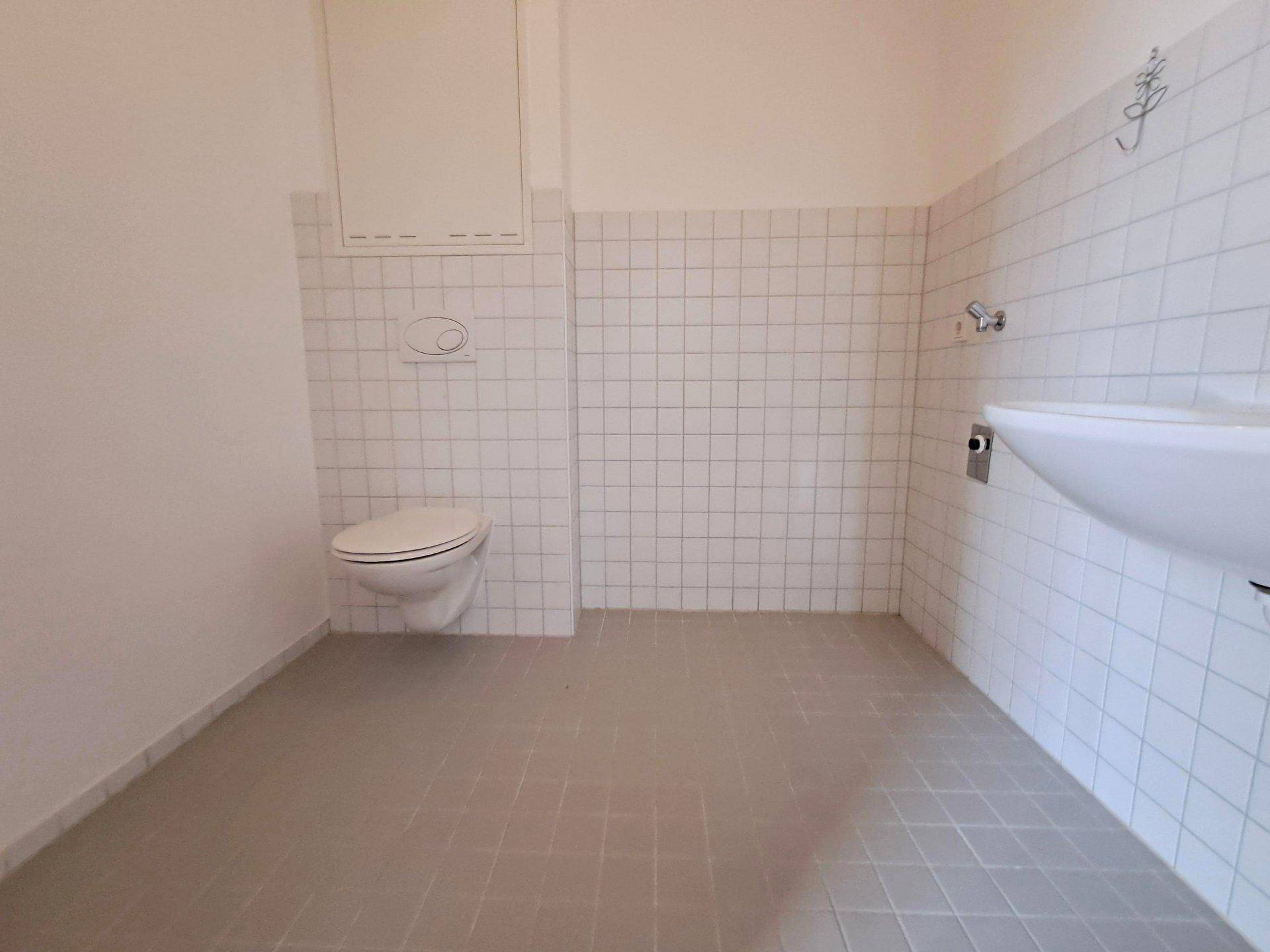 Separates WC mit wandhängender Toilette, Waschbecken und weißen Fliesen.