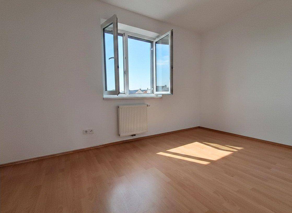 Helles Zimmer mit Laminatboden und einem geöffneten Fenster, das frische Luft hereinlässt.