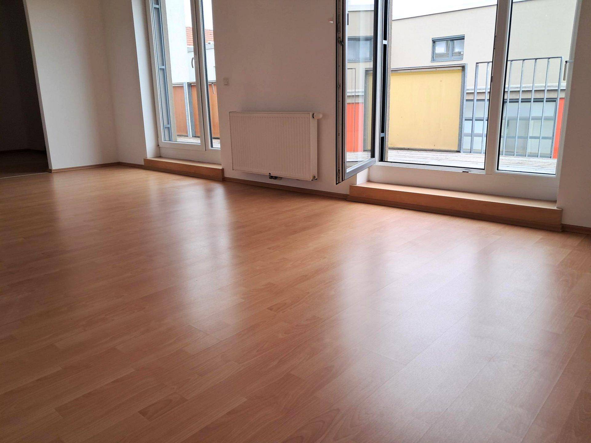 Heller Wohnbereich mit Laminatboden und Zugang zu einem Außenbereich durch große Fenstertüren.