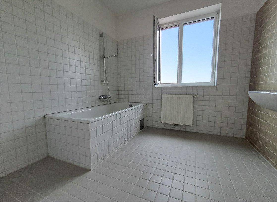 Badezimmer mit weiß gefliesten Wänden, Badewanne und Fenster für natürliche Belüftung.