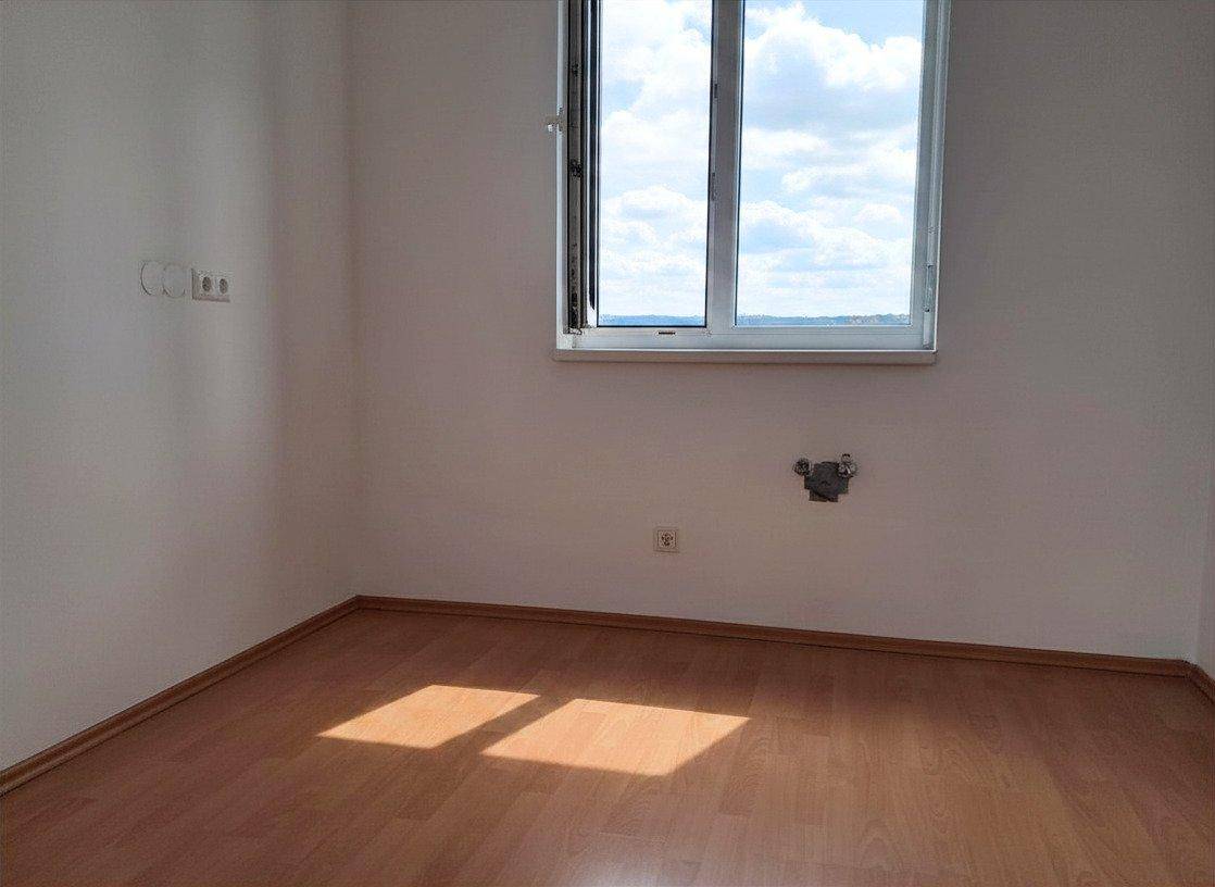 Leeres Zimmer mit Laminatboden und einem Fenster, das viel Tageslicht hereinlässt.