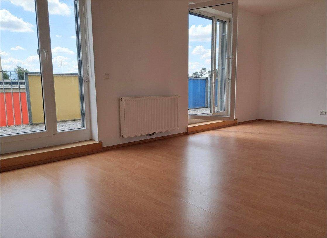 Geräumiges Zimmer mit Laminatboden und großen Fenstertüren, die zu einem Balkon führen.