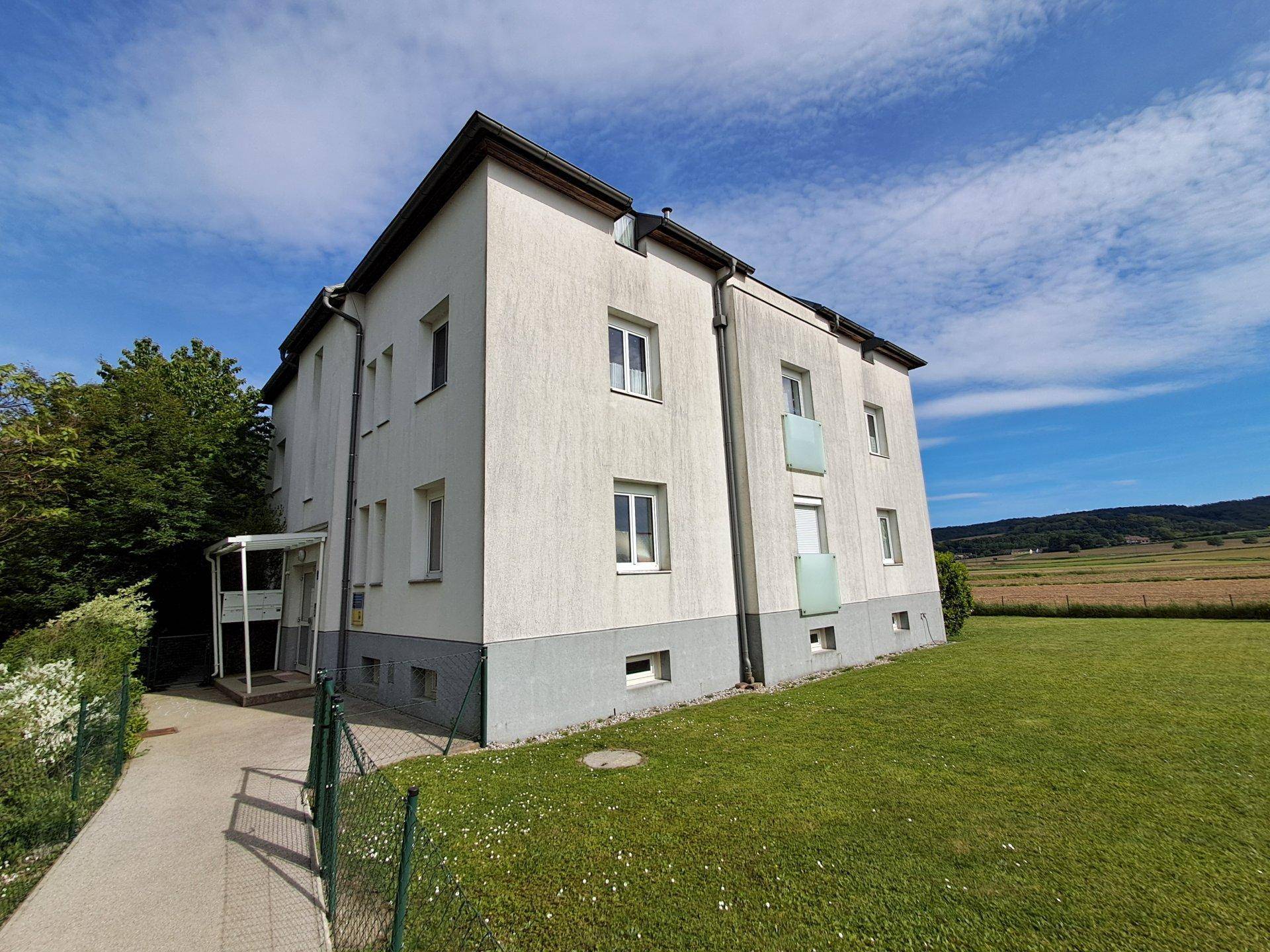 Seitenansicht des Mehrfamilienhauses mit Balkonen und weitem Blick auf die angrenzenden Felder und Natur.