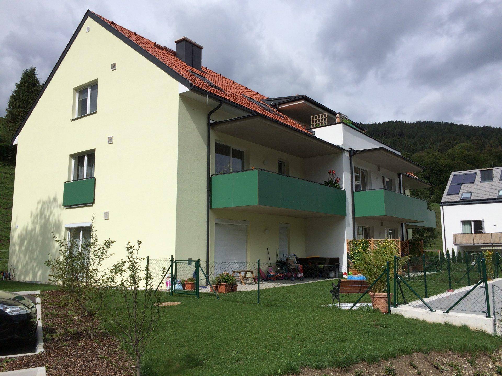Mehrfamilienhaus mit hellgrüner Fassade, roten Dachziegeln und Balkonen in ländlicher Umgebung.