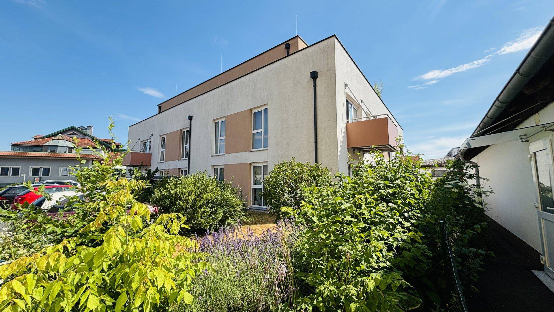 Moderne Wohnanlage mit heller Fassade, Balkon und gepflegter Bepflanzung im Außenbereich.