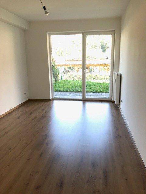 Heller Wohnraum mit Laminatboden, Heizkörper und großer Glasschiebetür zum Garten.