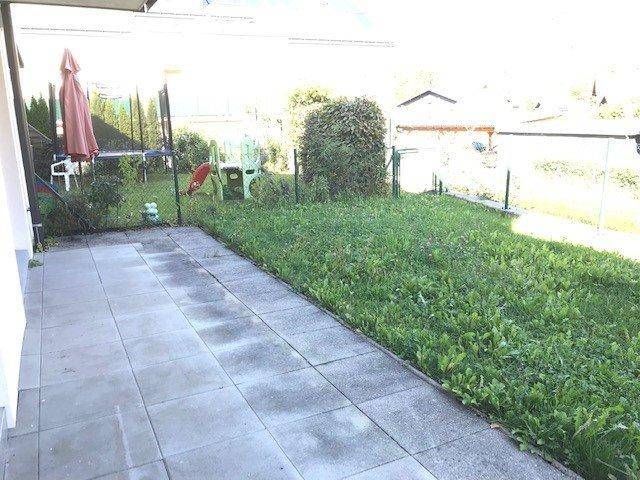 Sonniger Terrassenbereich mit Pflastersteinen, Rasen und einem Sonnenschirm für entspannte Stunden im Freien.