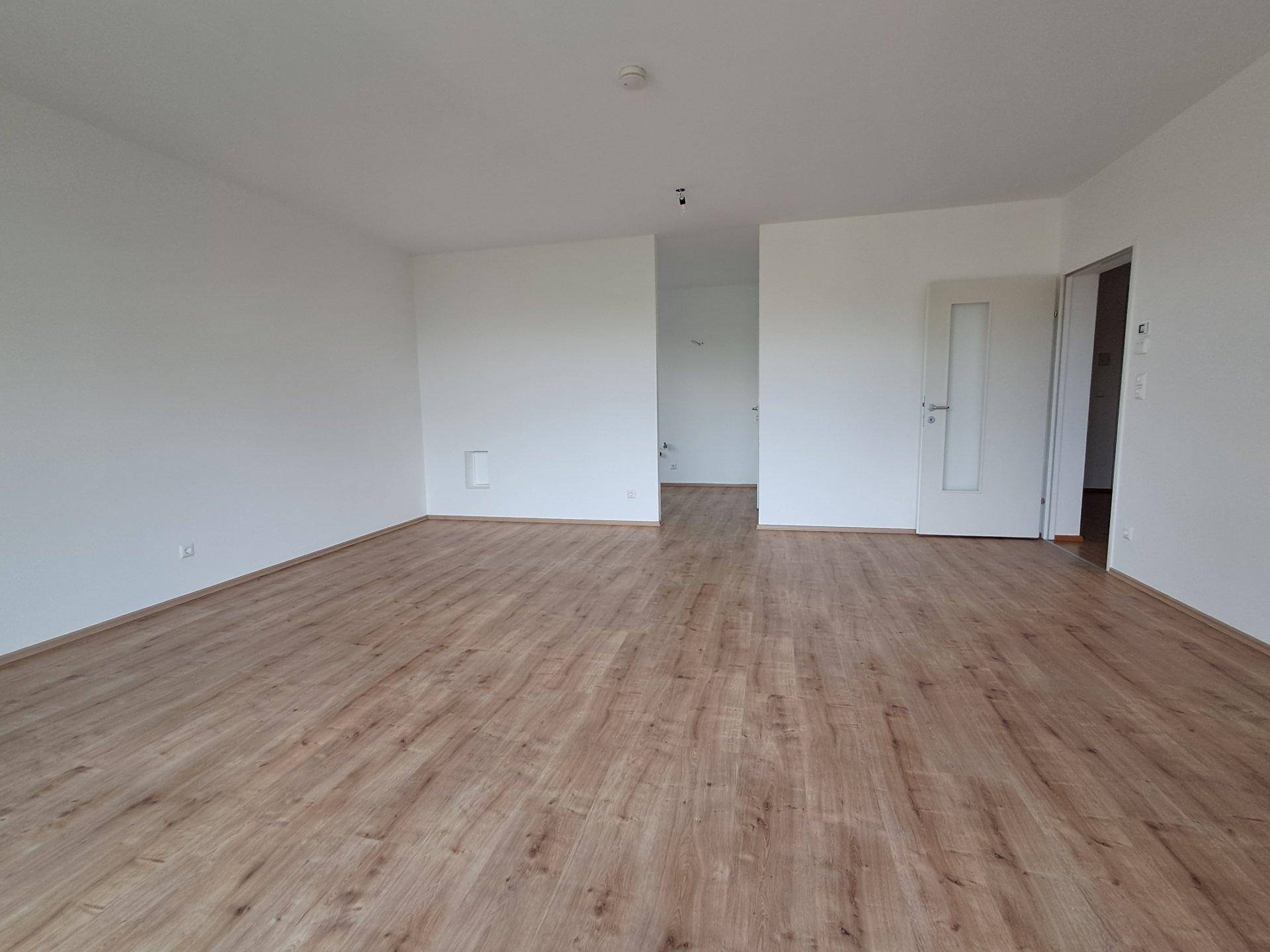 Helles, leeres Wohnzimmer mit Laminatboden und weißen Wänden, bereit zur individuellen Gestaltung.