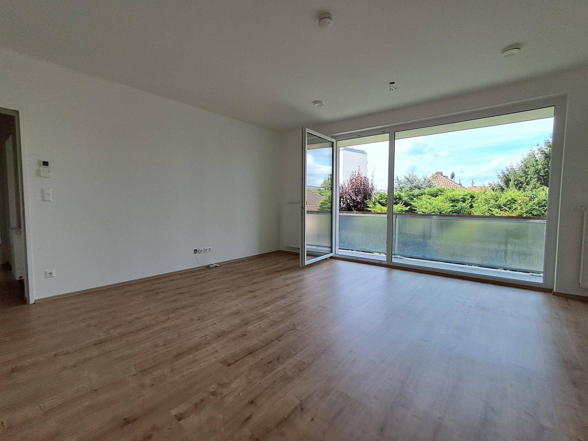 Geräumiges Wohnzimmer mit Laminatboden, weißen Wänden und großem Zugang zum Balkon.