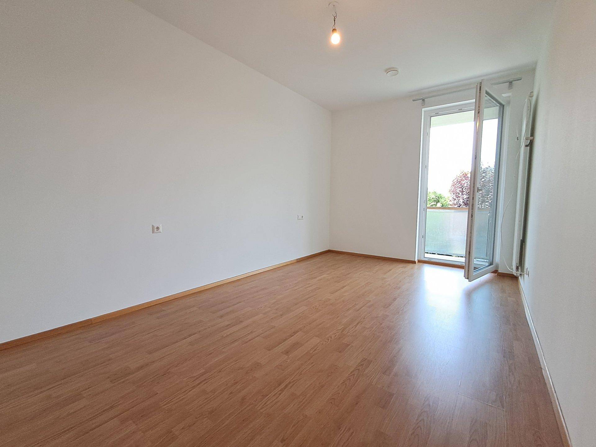 Helles Schlafzimmer mit Laminatboden, weißen Wänden und direktem Zugang zu einem Balkon.