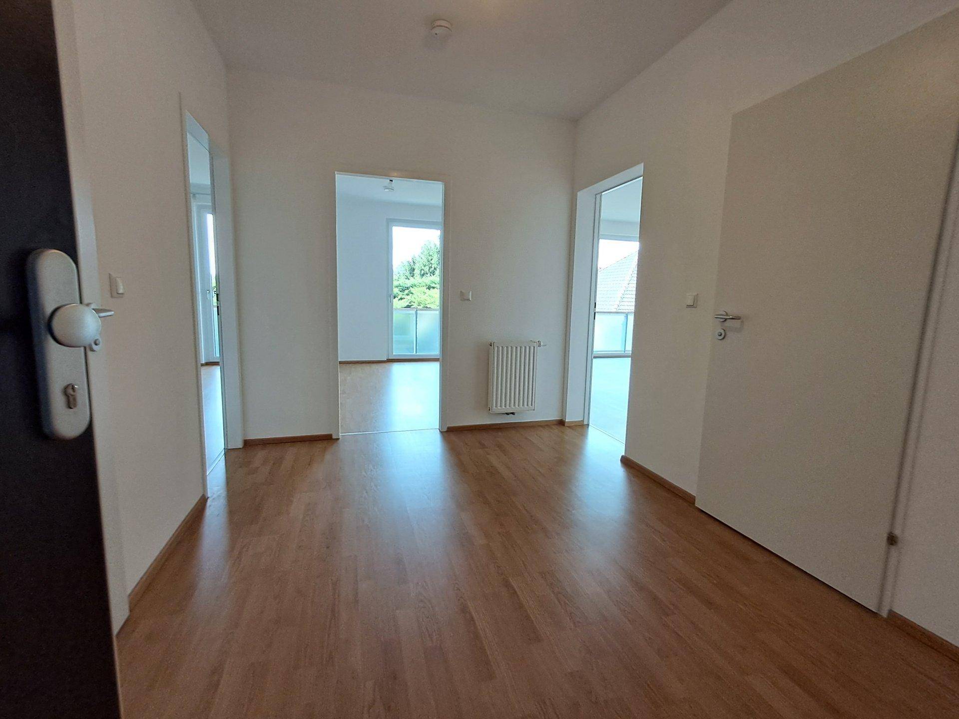 Heller Flur mit Laminatboden und weißen Wänden, der Zugang zu verschiedenen Räumen bietet.