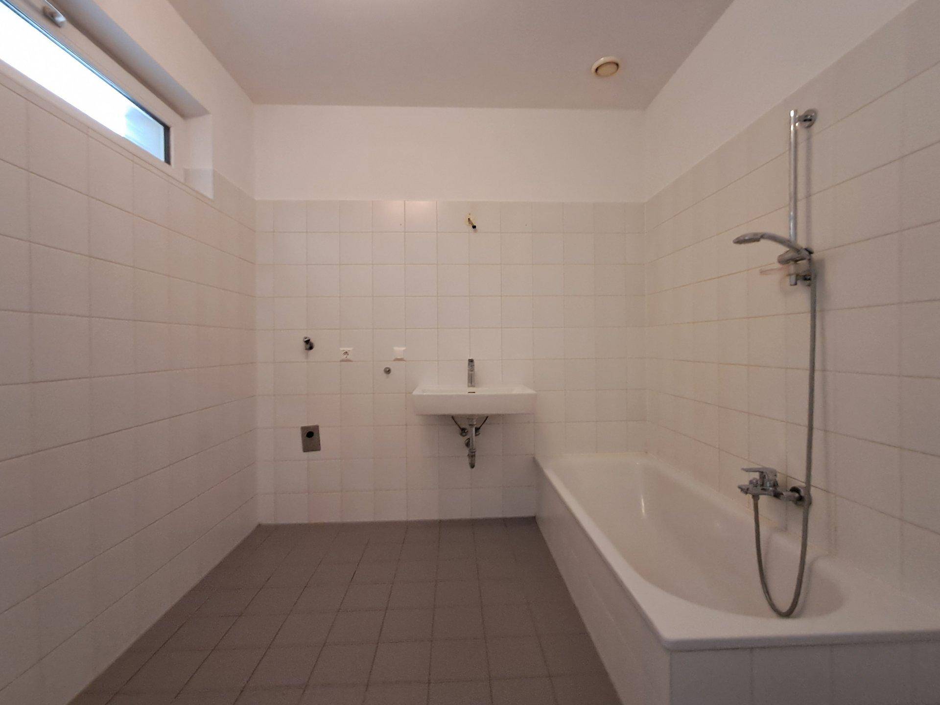 Modern gefliestes Badezimmer mit Badewanne, Duschfunktion, Waschbecken und einem kleinen Fenster.