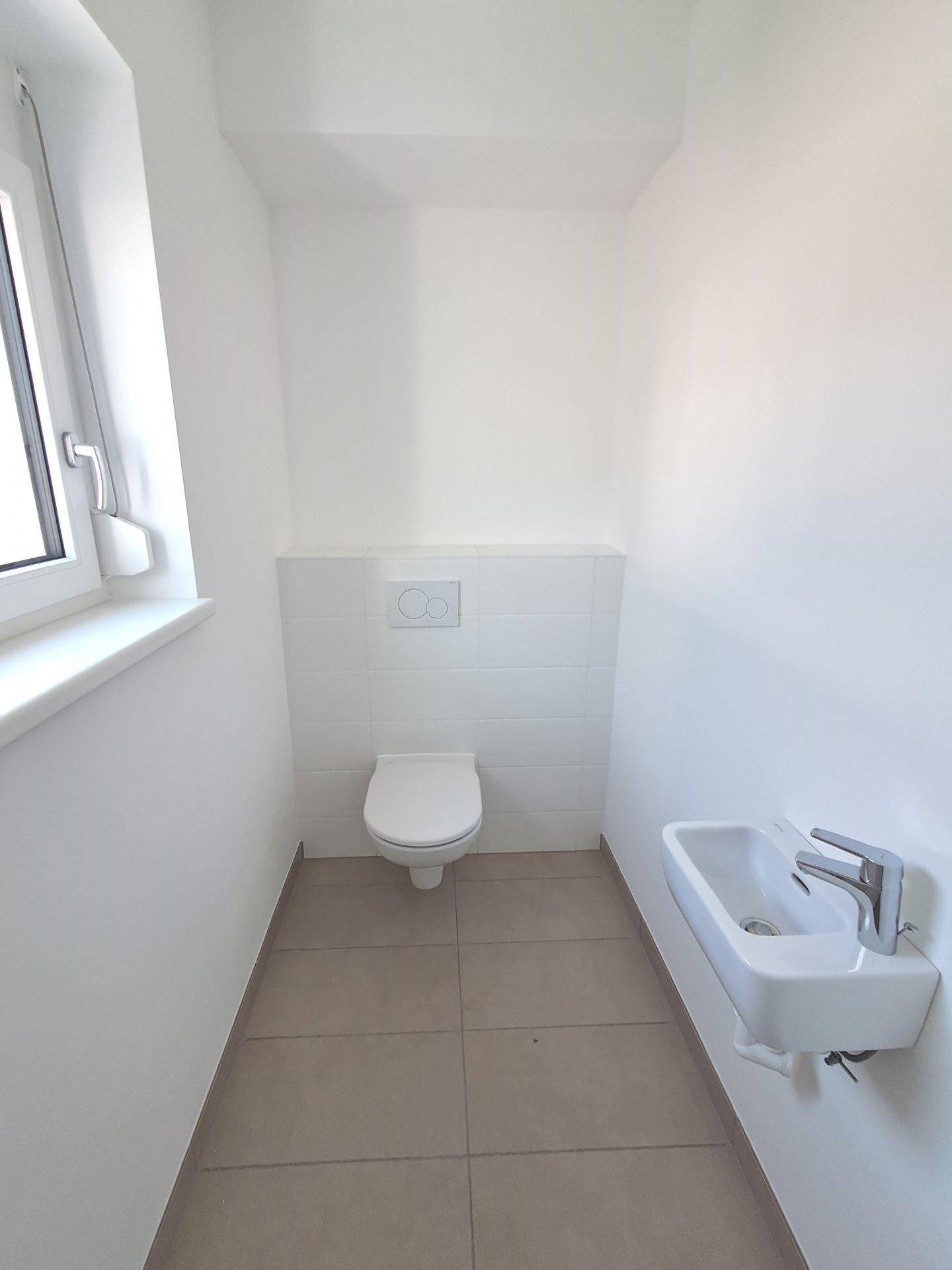 Kleines Gäste-WC mit wandhängendem WC, Handwaschbecken und Fenster.