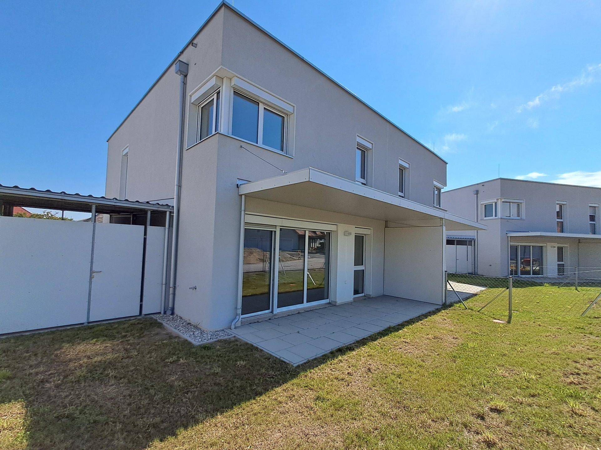 Moderne Hausfassade mit großer, unmöblierter Terrasse und angrenzender Rasenfläche.