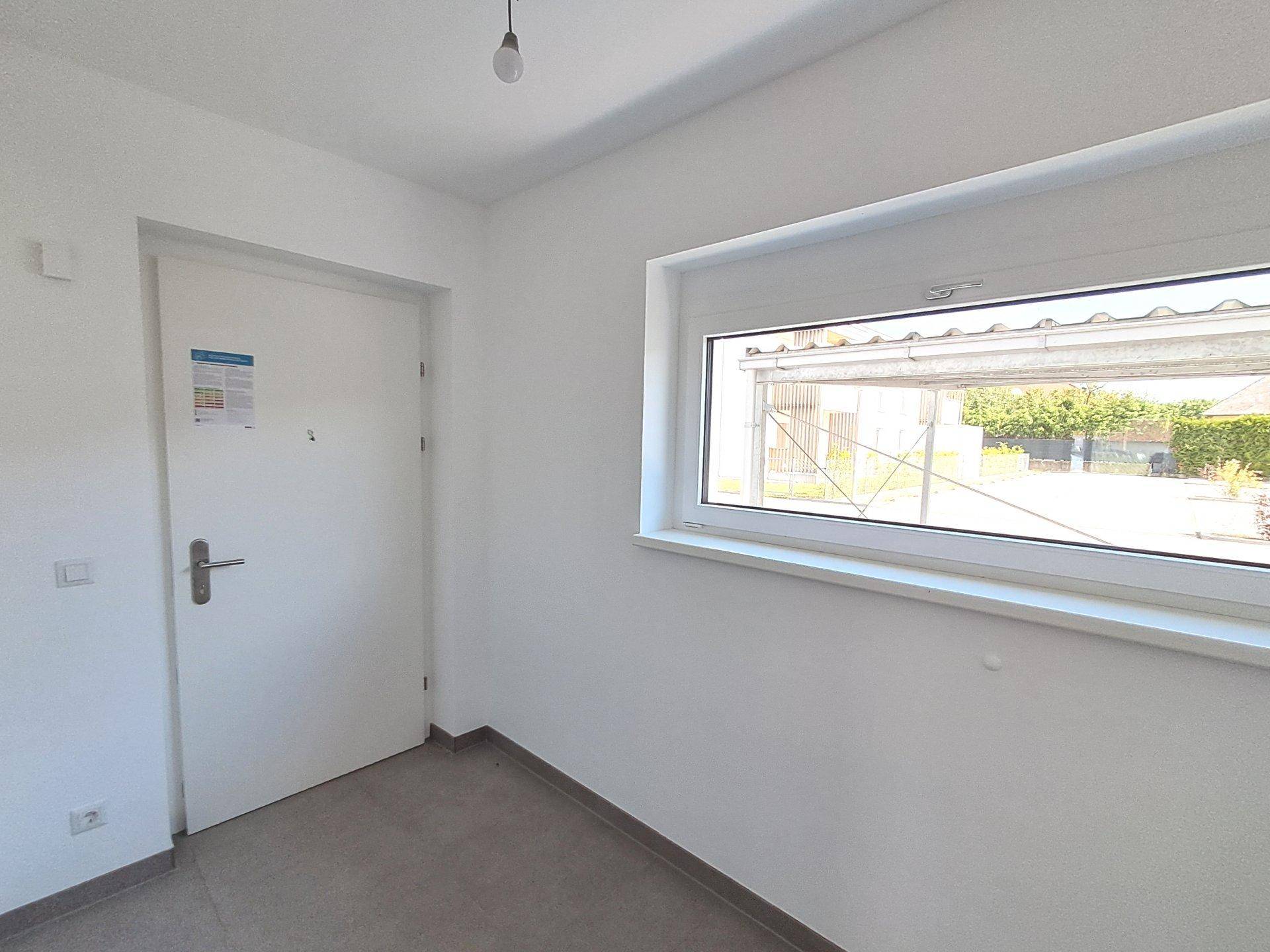 Heller Eingangsbereich mit weißer Tür, Fenster und neutralen Bodenfliesen.