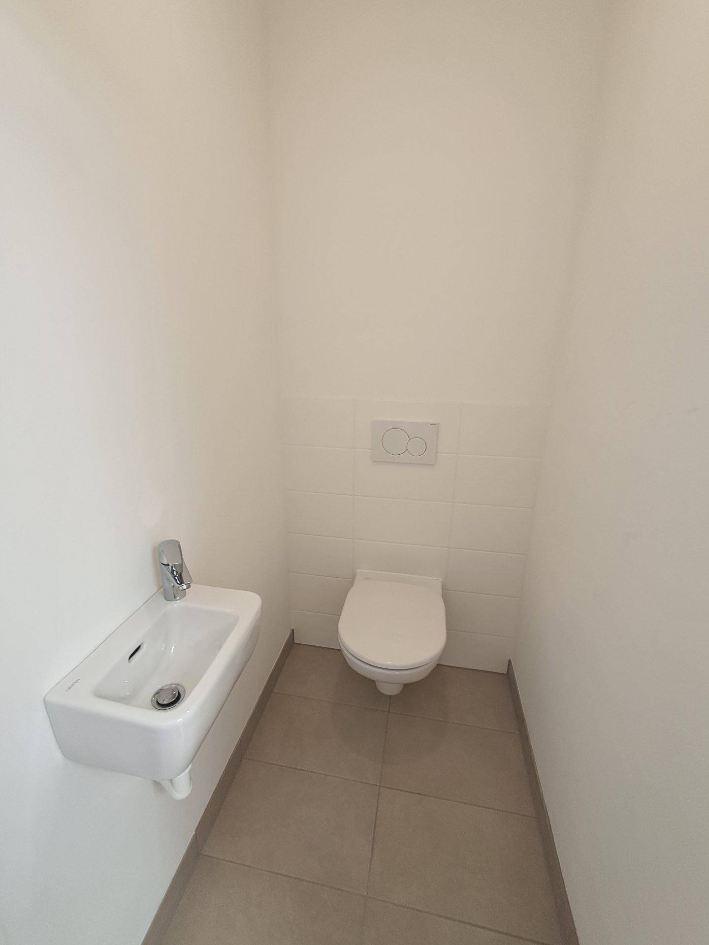 Kleines Gäste-WC mit wandhängendem WC, Handwaschbecken und neutralen Fliesen.