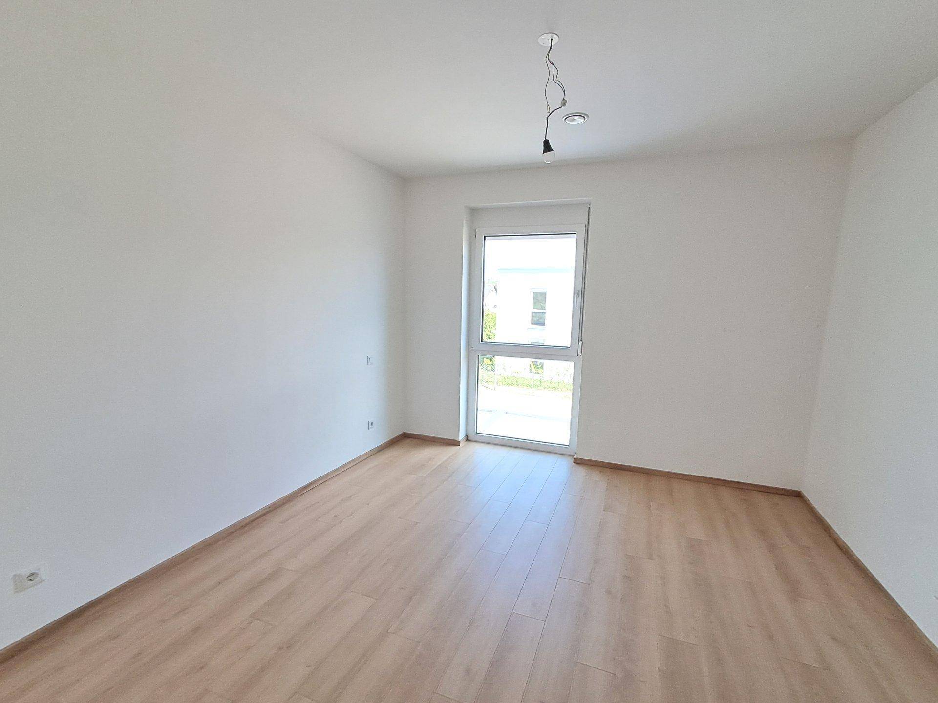 Leeres Schlafzimmer mit hellem Laminatboden und großem Fenster, bereit für persönliche Gestaltung.