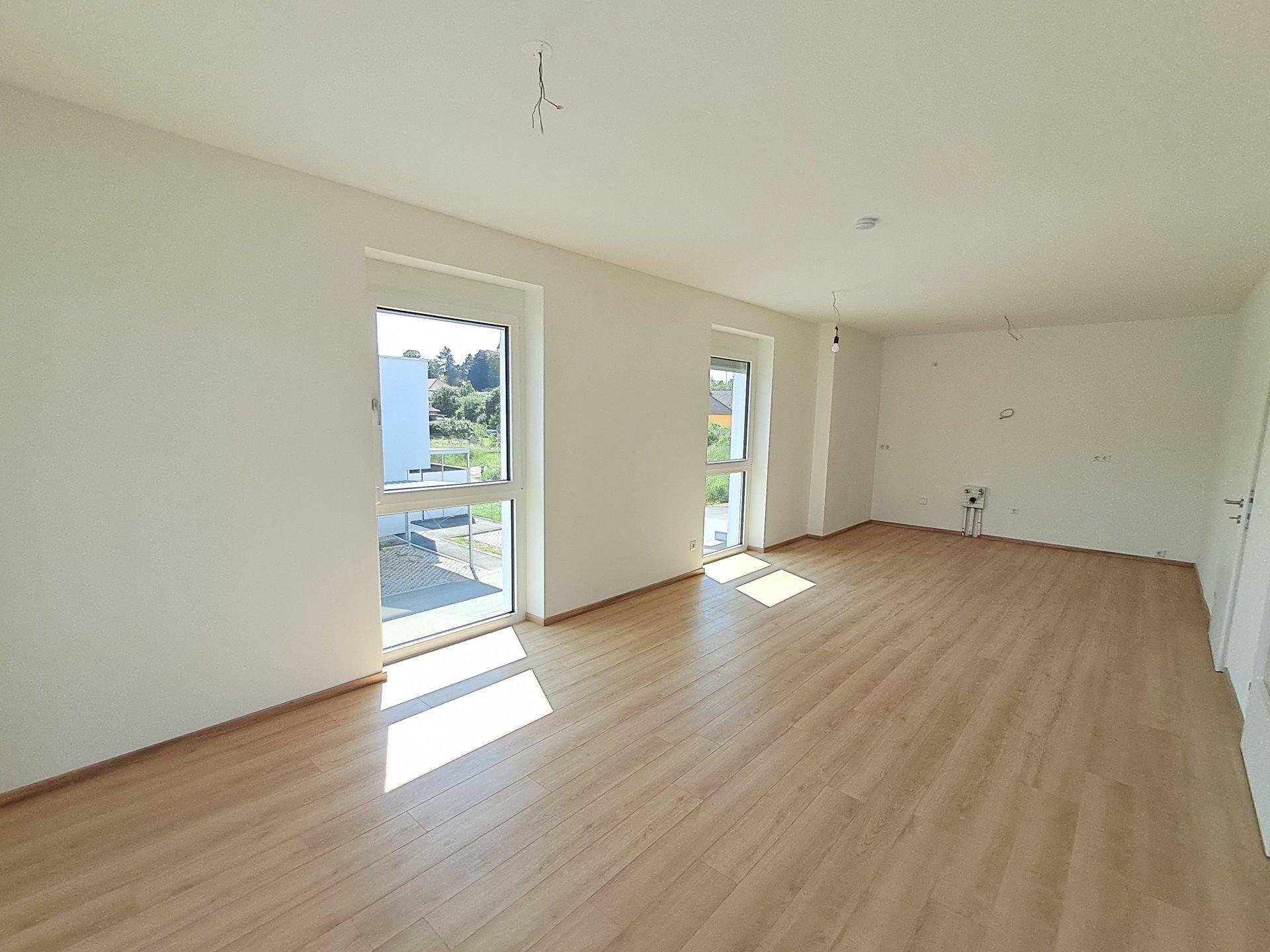 Lichtdurchfluteter Wohnraum mit großen Fenstern und hellem Laminatboden, bietet viel Potenzial zur Einrichtung.