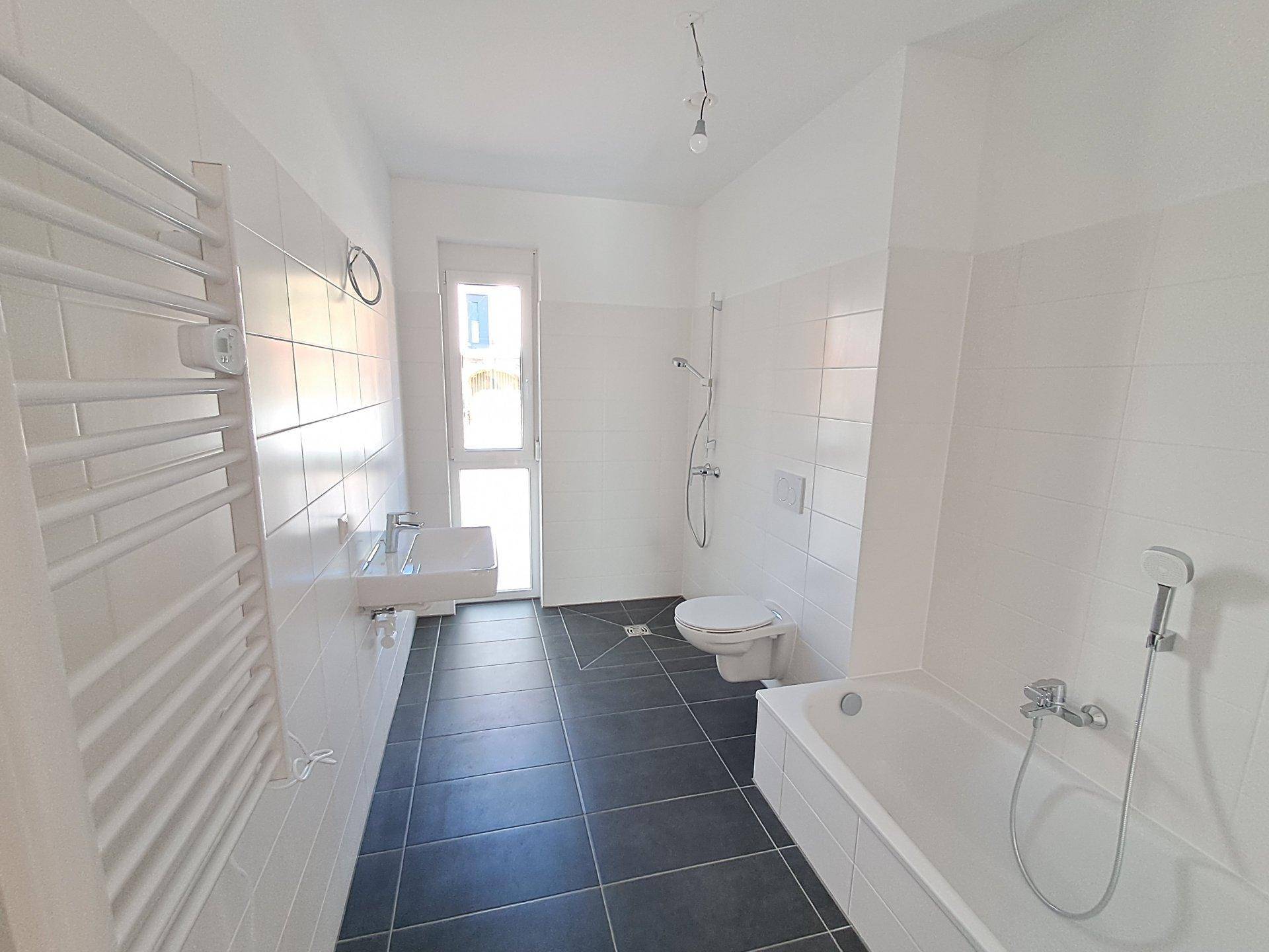 Unmöbliertes Badezimmer mit Badewanne, Dusche, Waschbecken und beheiztem Handtuchhalter.