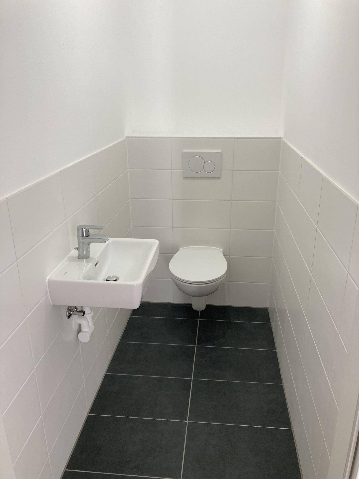 Kleines Gäste-WC mit Wand-WC, Waschbecken und weißen Fliesen.