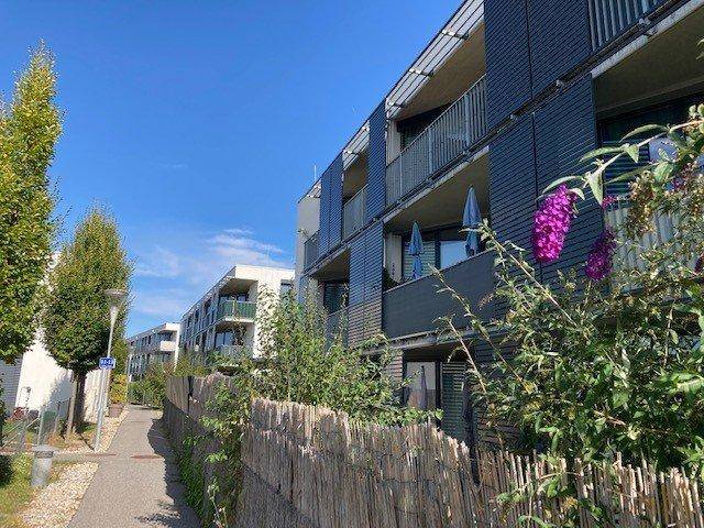 Moderne Fassade eines Wohngebäudes mit Balkonen entlang eines Fußwegs unter blauem Himmel.