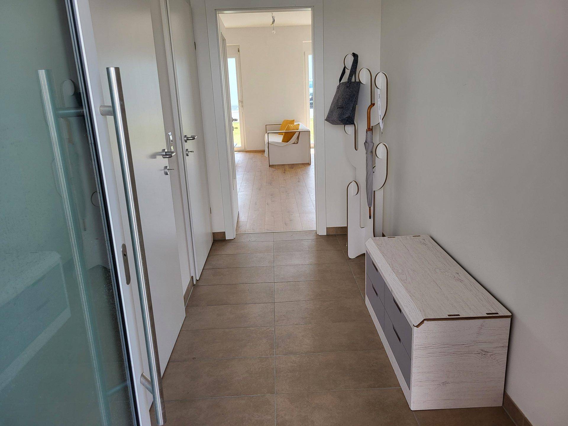 Heller Flur mit modernen Fliesen, einer Sitzbank und Garderobe, der zu weiteren Räumen führt.