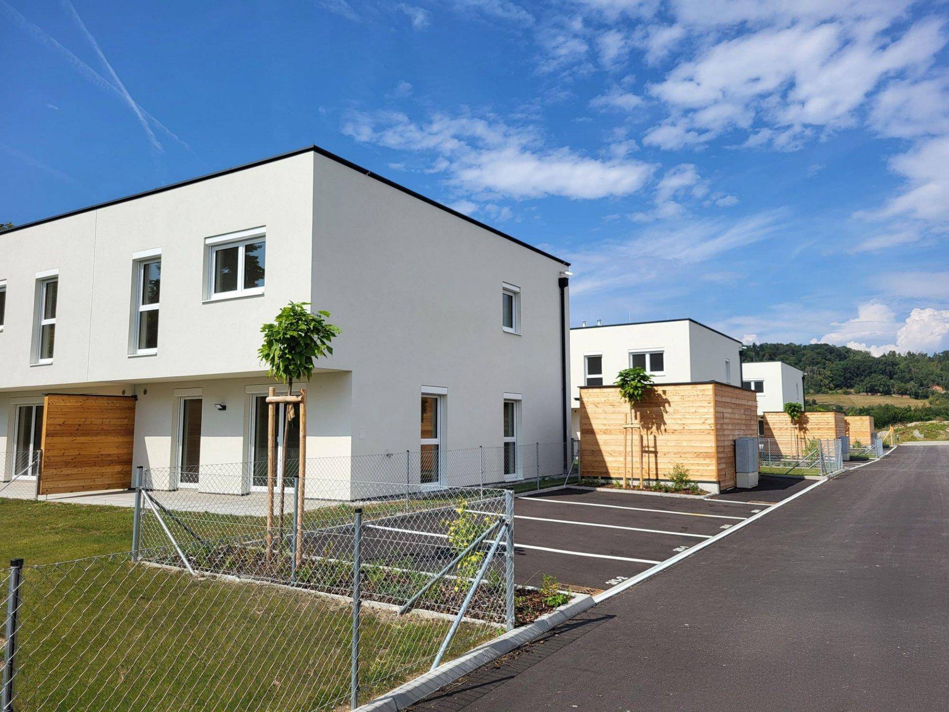 Reihe moderner Neubauten mit Parkplätzen und angrenzenden Grünflächen unter blauem Himmel.