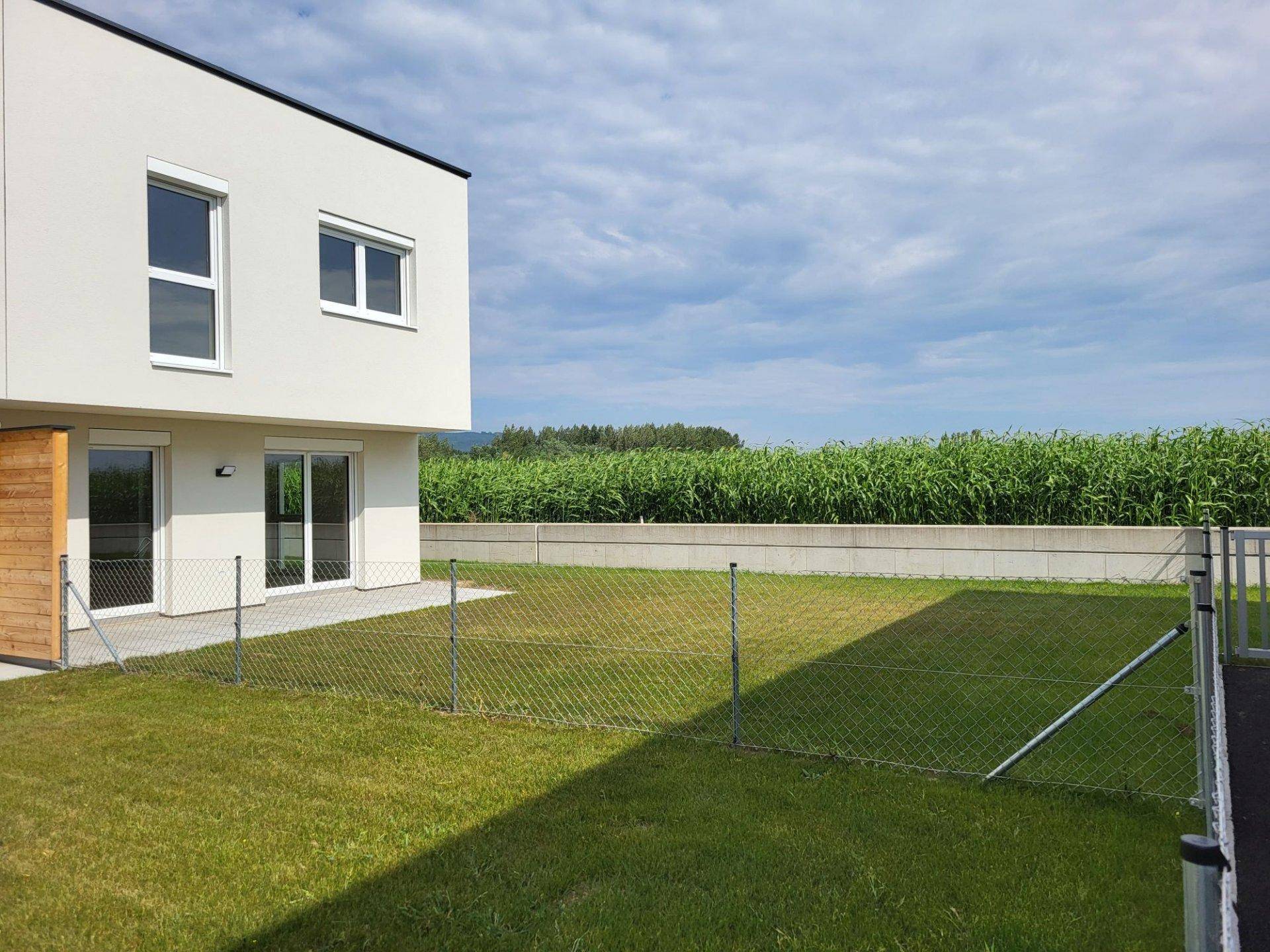 Seitlicher Blick auf das moderne Gebäude mit einem grünen Rasenbereich und angrenzendem Feld.