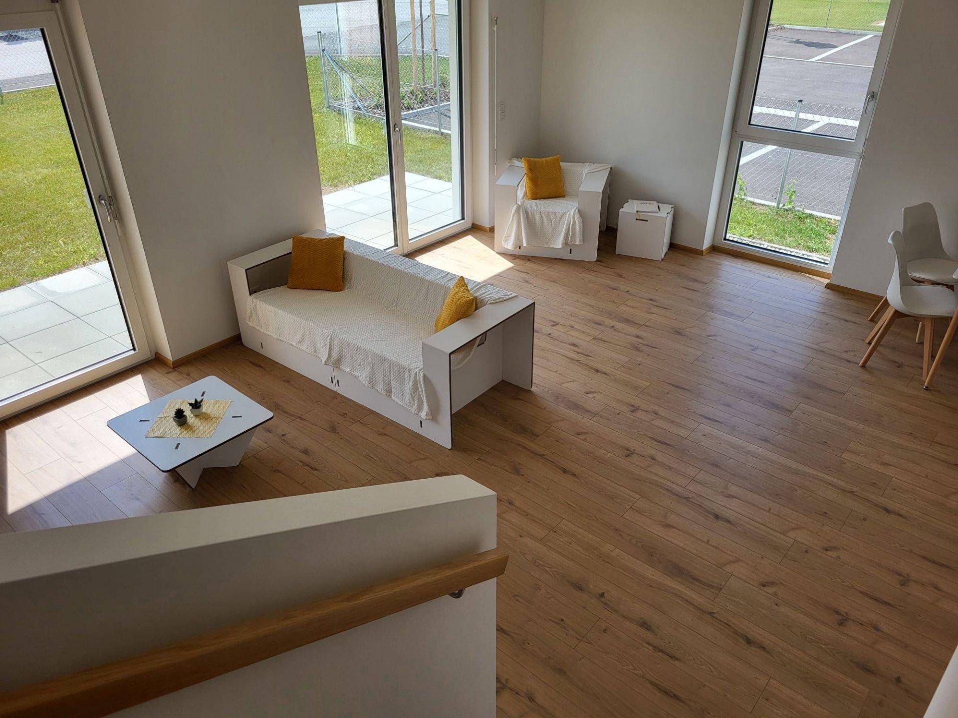 Heller Wohnbereich mit Laminatboden und großen Fenstern, die viel Tageslicht hereinlassen und Ausblick bieten.