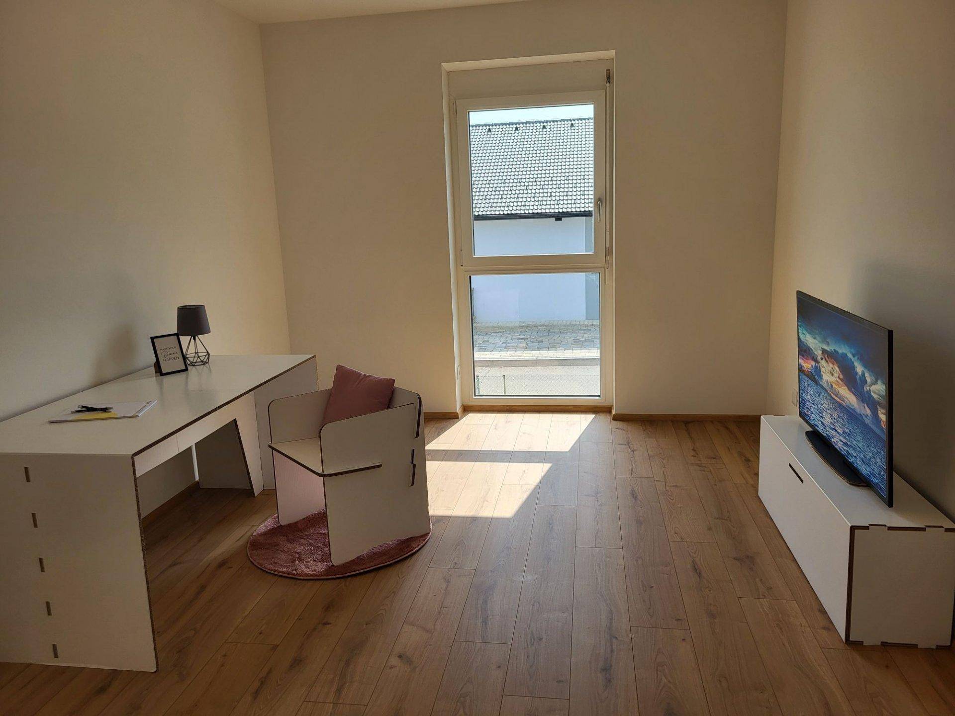 Funktionaler Arbeitsraum mit Laminatboden, Schreibtisch, Stuhl und großem Fenster für Tageslicht.