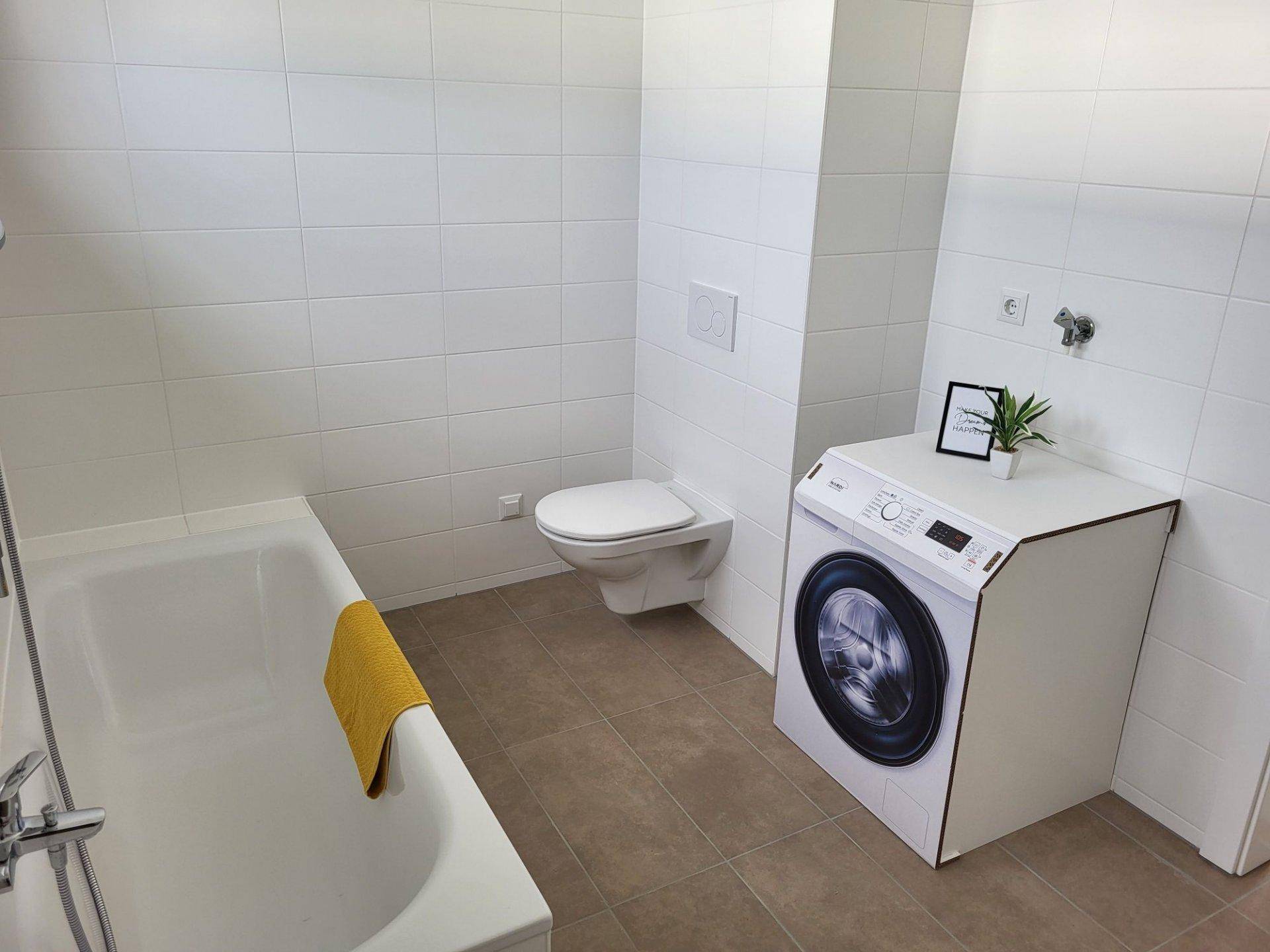 Modernes Badezimmer mit weißen Fliesen, Badewanne, wandhängendem WC und Platz für eine Waschmaschine.