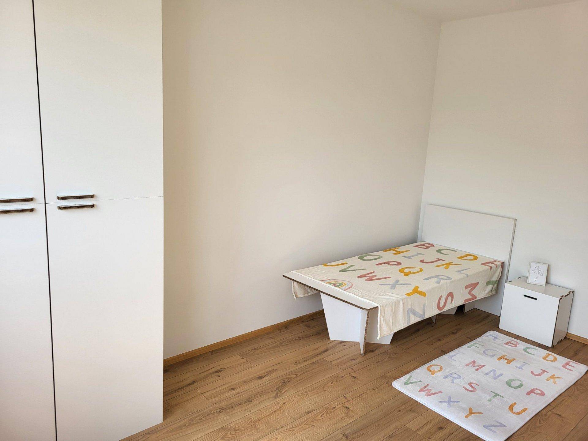 Kinderzimmer mit Laminatboden, Einzelbett, weißem Kleiderschrank und einem bunten Teppich.
