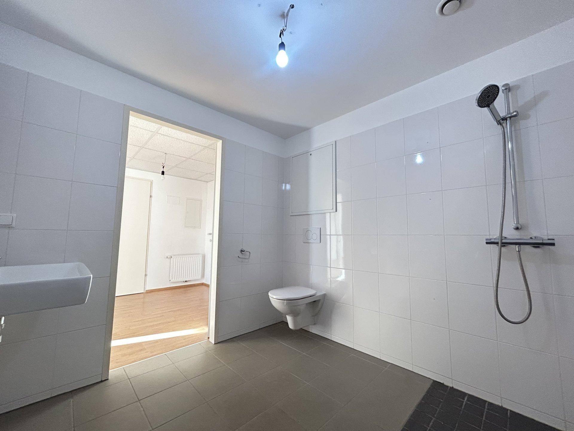 Modern gefliestes Badezimmer mit Dusche, wandhängendem WC und Waschbecken in hellen Farben.