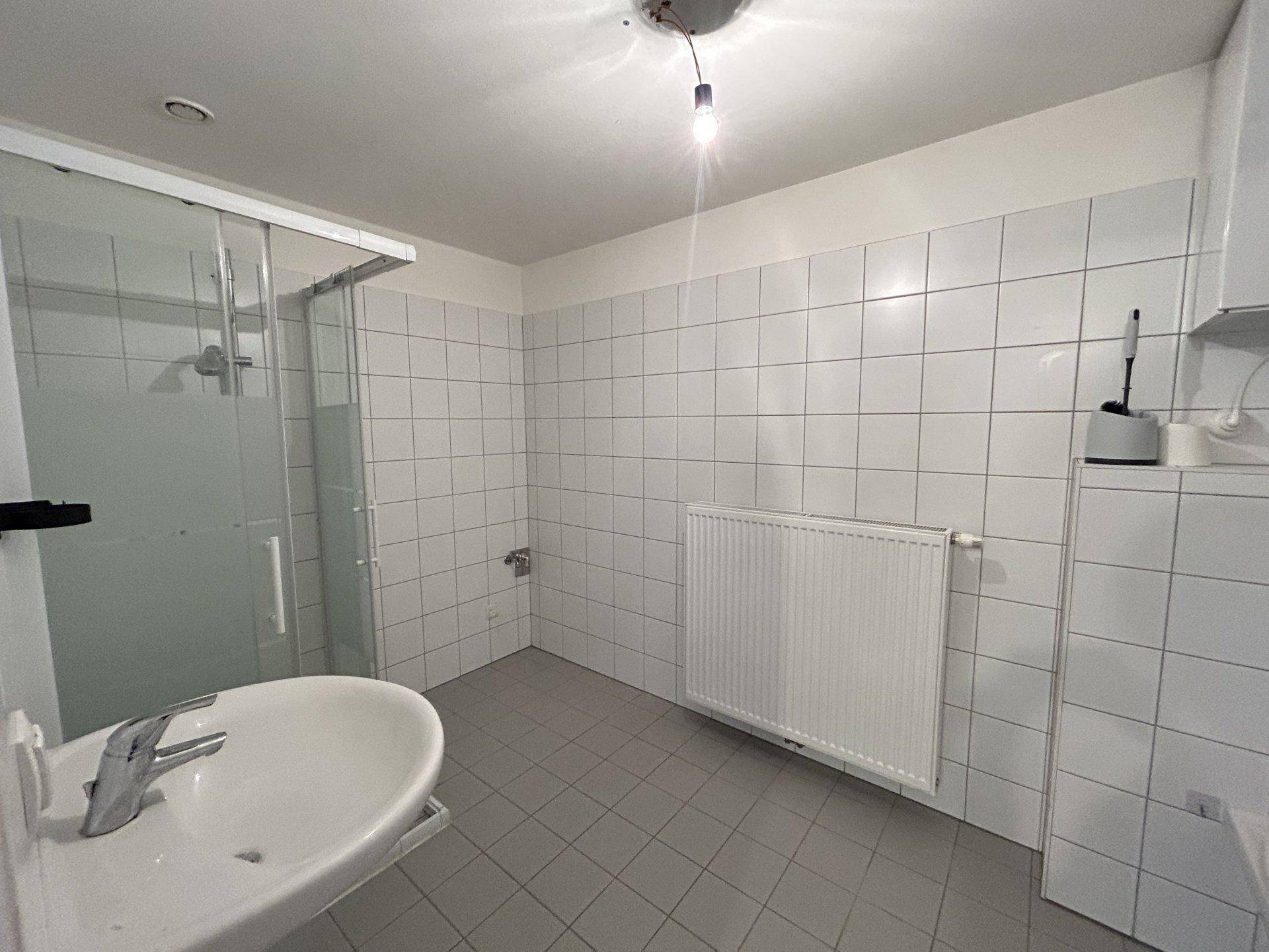 Helles Badezimmer mit Duschkabine, Waschbecken und weißen Wandfliesen.